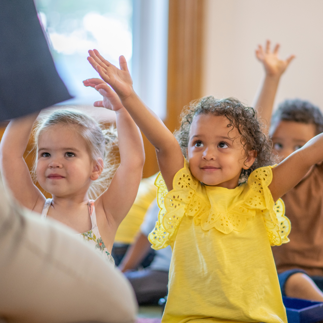 Children with arms raised during story time.