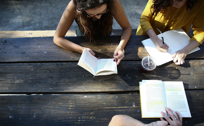 Three people sitting at picnic table with books